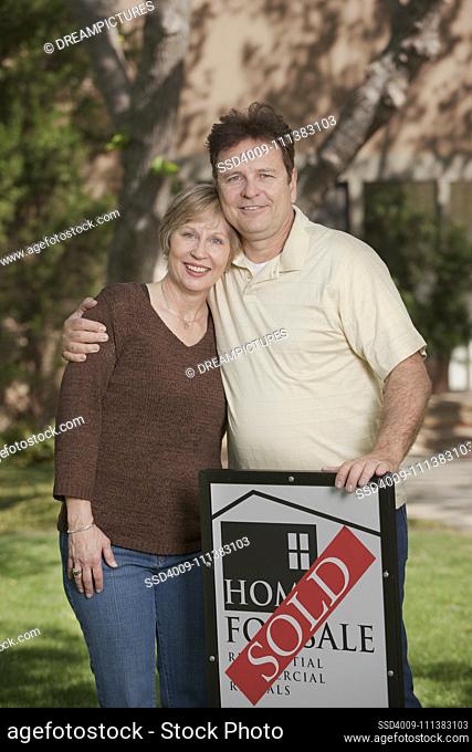 Couple standing in yard with sold sign