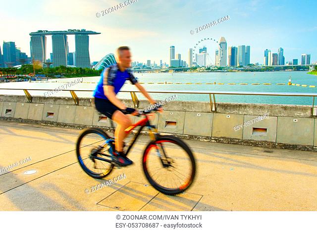 Man riding a bicycle in Singapore bay at sunset