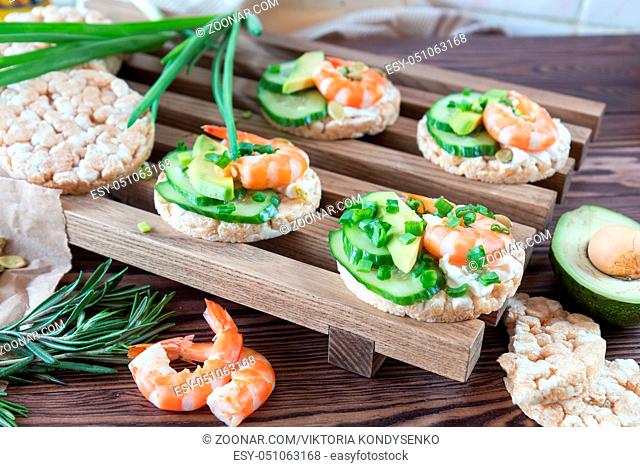 Rice cakes with sliced avocado cucumber shrimp and cream cheese. Fresh parsley and rosemary. Vegetarian, vegan concept. Shallow depth of field
