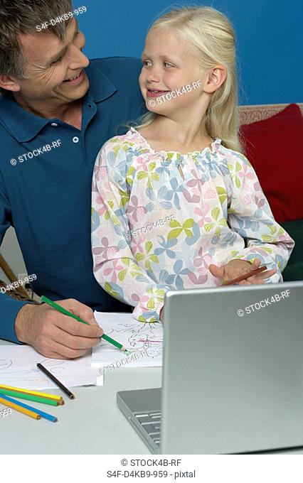 Man sitting behind a laptop with his daughter while drawing in a sketchbook