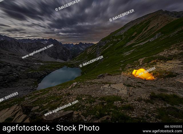 Tent in mountainous landscape with Lake Guffelsee in moonlight and cloudy sky, Gramais, Lechtal Außerfern, Tyrol, Austria, Europe