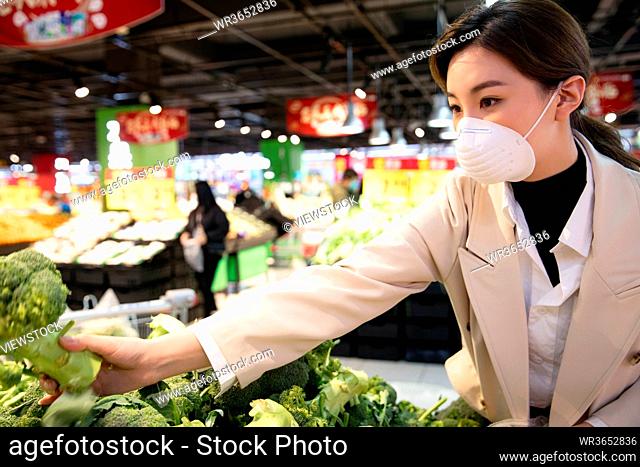 Wearing a mask of the young woman buy vegetables in the supermarket