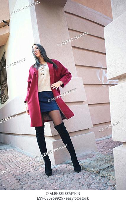 young beautiful stylish woman walking in burgundy coat, street style, spring summer trend, dark skirt, beige jacket, flirty