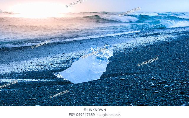 Icebergs sphashed by sea waves on black beach at sunrise time near Jokulsarlon glacier lake, Iceland