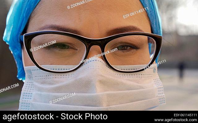 Tired Doctor During Coronavirus Or Covid-19 Virus Epidemic, Female Practice Medic In Protective Mask, Cap And Eyeglasses Looking Seriously At Camera