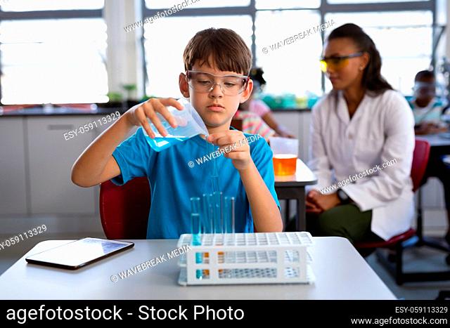 Caucasian boy pouring chemical from beaker into the test tube in science class at laboratory