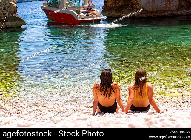 Two beautiful young woman's friends sitting on the beach, talking and having rest. sea rocky beach, copy space