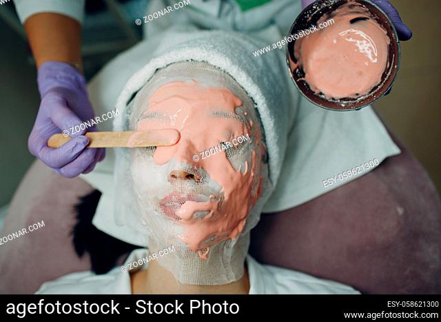 Alginate face mask application process. A female hands of a beautician holding spatula. Woman lying on a couch in office of cosmetologist
