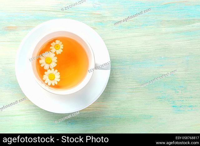 An overhead photo of a cup of chamomile tea on a teal blue background with copyspace
