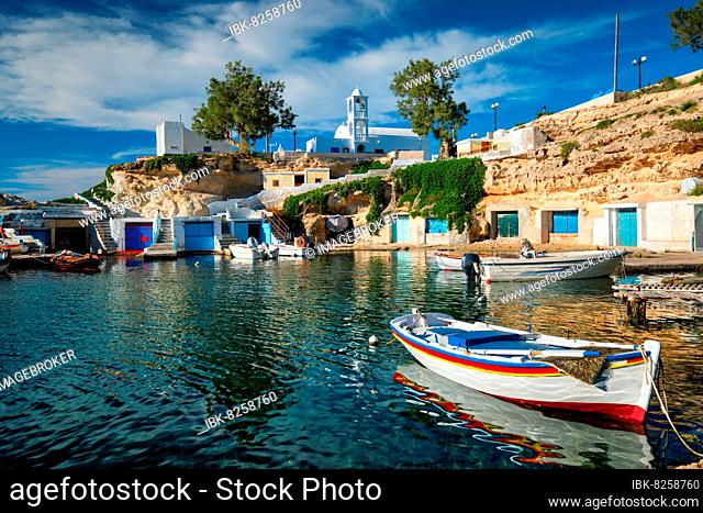 Fishing boats moored in crystal clear turquoise sea water in harbour in Greek fishing village of Mandrakia, Milos island, Greece, Europe