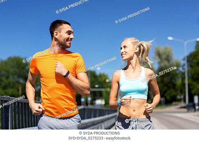 couple with fitness trackers running along bridge