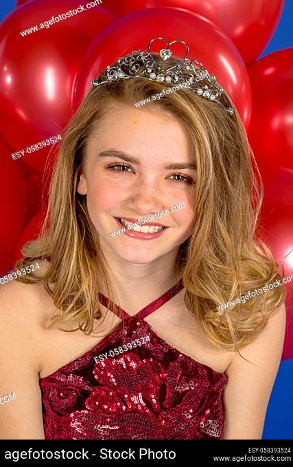 A beautiful blonde teenage model posing in a tiara and red balloons in front of the camera in a studio environment