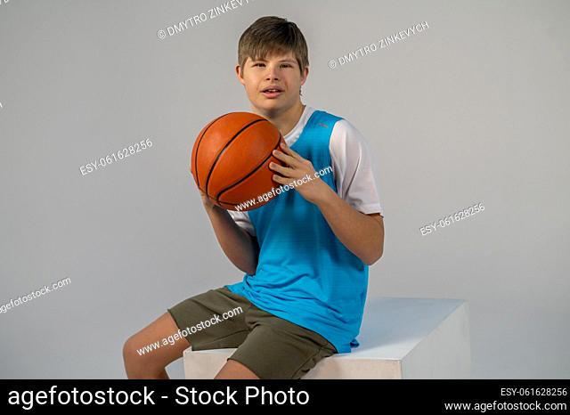 Basketball. Boy in shorts and blue tshirt sitting with a basket ball