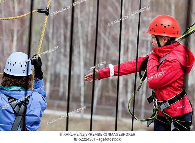 10-year-old girl reaching out to somebody climbing in a high rope course, Berlin, Germany, Europe