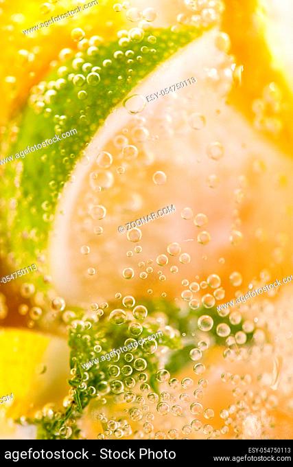 Macro photo of freshly made lemonade with pieces of lime, lemon and bubbles in a glass. Summer refreshing drink