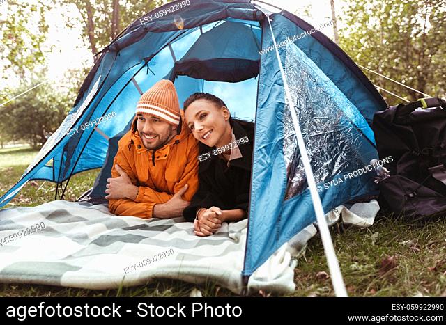 happy couple lying inside tent at campsite