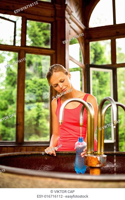 Young woman fillig a plastic bottle with healthy mineral water from a wellspring in a spa (shallow DOF)