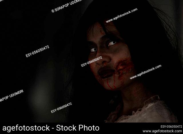 Female zombie in blood. Closeup face and eyes of Asian Woman ghost with blood. Horror creepy scary fear in a dark house. Hair covering the face