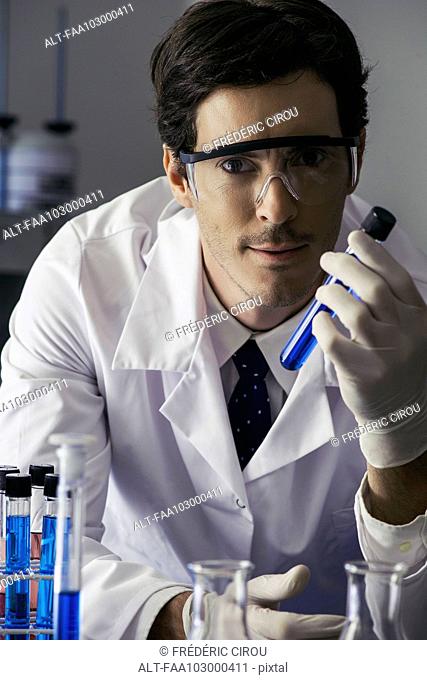 Scientist holding test tube in lab, looking at camera with determined expression