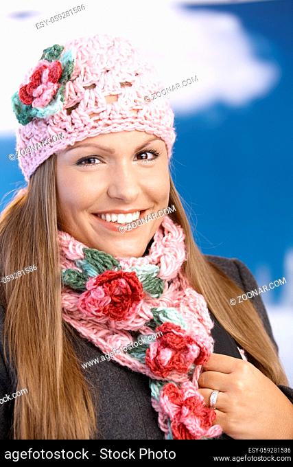 Pretty young girl dressed up warm in coat, cap and scarf, smiling front of winter landscape