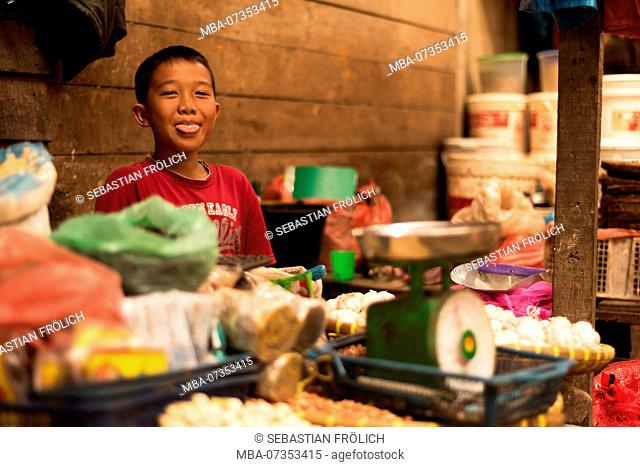 A little boy selling vegetables and spices at a market stall and laughs, or sticking out his tongue