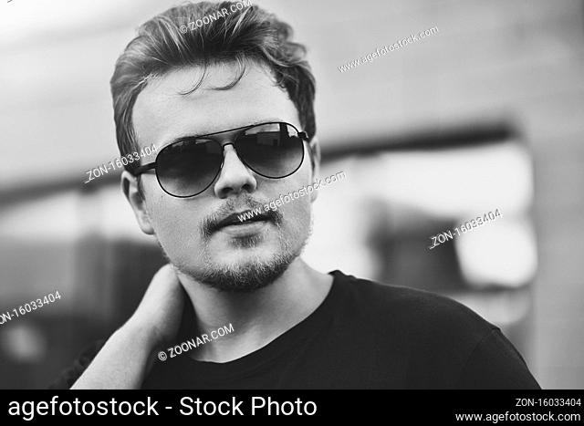 Handsome stylish man with sunglasses and modern hairstyle and beard. Outdoor in the street. black and white photo