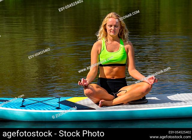 Young caucasian woman meditating on SUP in dutch river