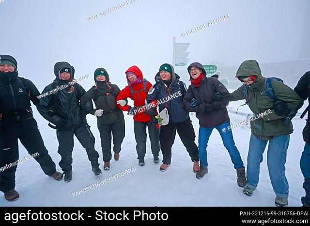 16 December 2023, Saxony-Anhalt, Schierke: Hikers stand on the Brocken in the early hours of the morning and sing a song together at the Brocken breakfast with...