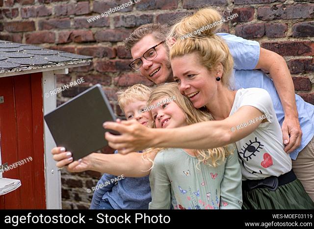 Smiling woman taking selfie with family through digital tablet at back yard