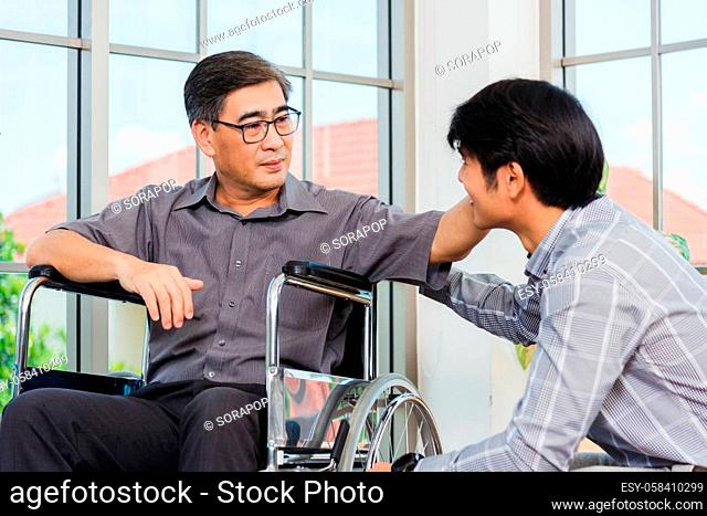 Asian senior disabled businessman in wheelchair discuss interacting together with the team in the office. The old man in a wheelchair and his young son talking...