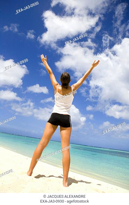 Woman standing on beach with arms raised