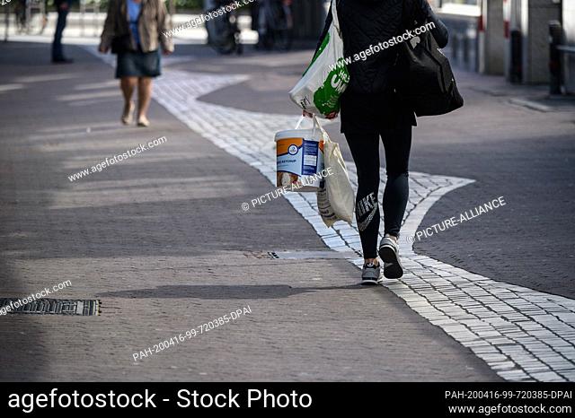 16 April 2020, Rhineland-Palatinate, Mainz: A woman walks through the city centre with shopping bags. On 15.04.2020, the federal and state governments agreed on...