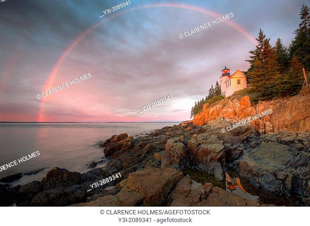 A double rainbow appears briefly at sunrise over Bass Harbor Head Lighthouse, which is reflected in a tidal pool as it overlooks the entrance to Bass Harbor and...