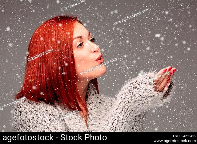Beautiful young girl with red hair and red nails holding her hands together and blowing on white lightening ball. Pretty woman in grey sweater catching star and...