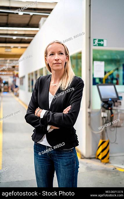 Confident blond female entrepreneur with arms crossed standing in industry