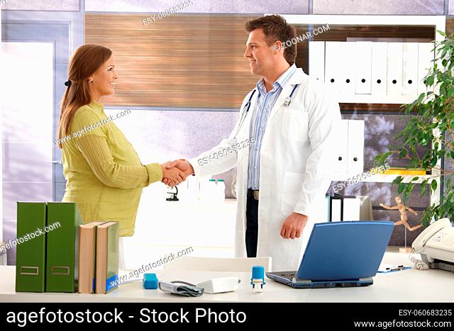Smiling pregnant woman shaking hands with doctor in consulting room