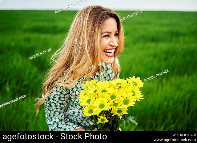 Happy woman looking away while holding yellow flowers at meadow