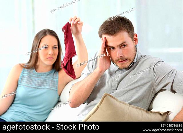 Disloyal cheater boyfriend caught by girlfriend showing underwear of another girl on a couch at home