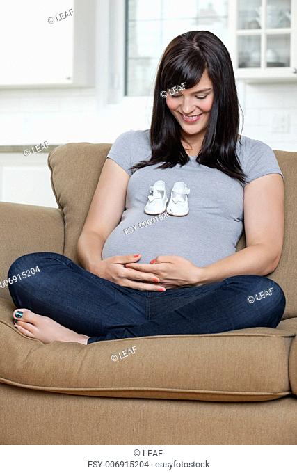 Happy pregnant woman looking at baby shoes on her belly
