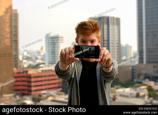 Portrait of young handsome teenage boy against view of the city outdoors