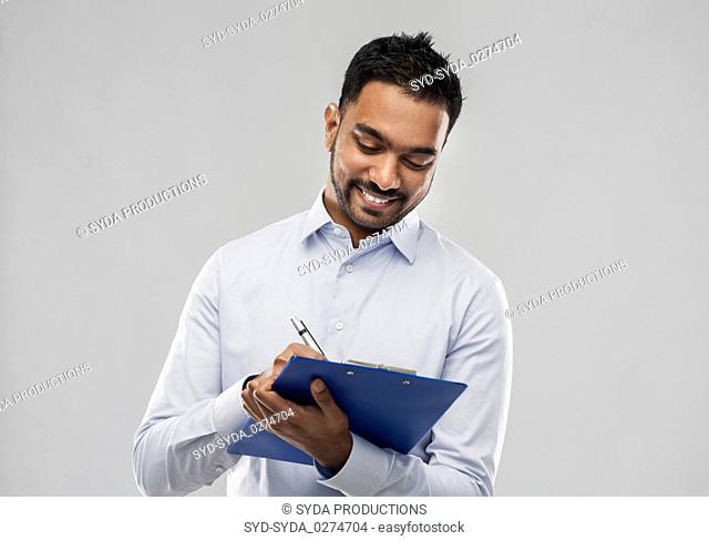 smiling indian businessman writing to clipboard