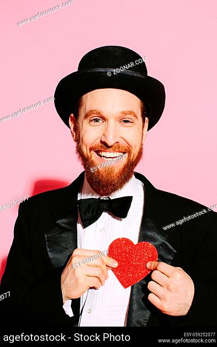 Happy man in a tuxedo and top hat holding a red heart