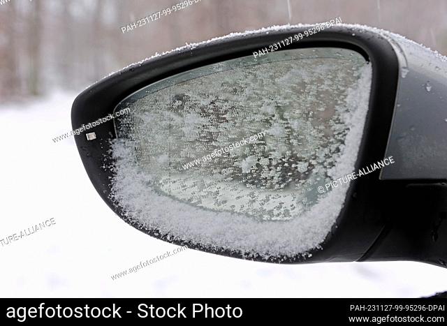 27 November 2023, Saxony-Anhalt, Benneckenstein: The side mirror of a vehicle in Benneckenstein is covered in snow. Widespread snowfall began in the Harz...
