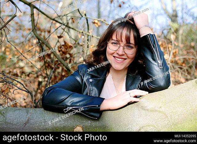 Laughing young woman leaning against tree trunk in forest