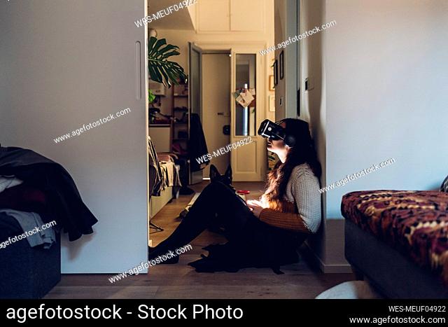 Woman with virtual reality headset sitting by wall at home