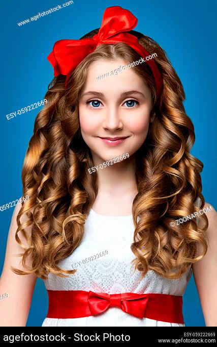 Beautiful teenage girl with curly hair and red rebbon looking like doll. Over blue backgroound