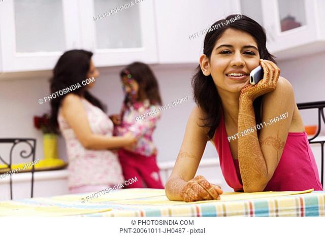 Portrait of a young woman talking on a mobile phone and a mid adult woman standing with her daughter in the background