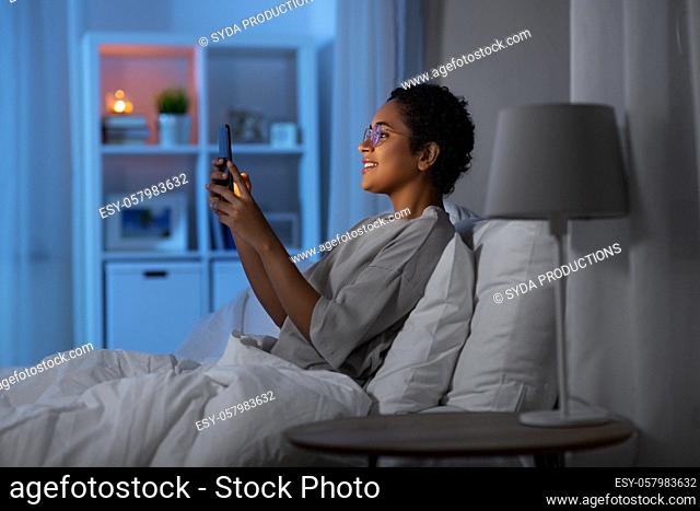 african woman with smartphone in bed at night