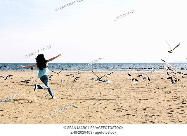 A young woman chasing after birds on a beach
