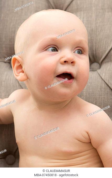 Baby sits naked on the sofa, portrait
